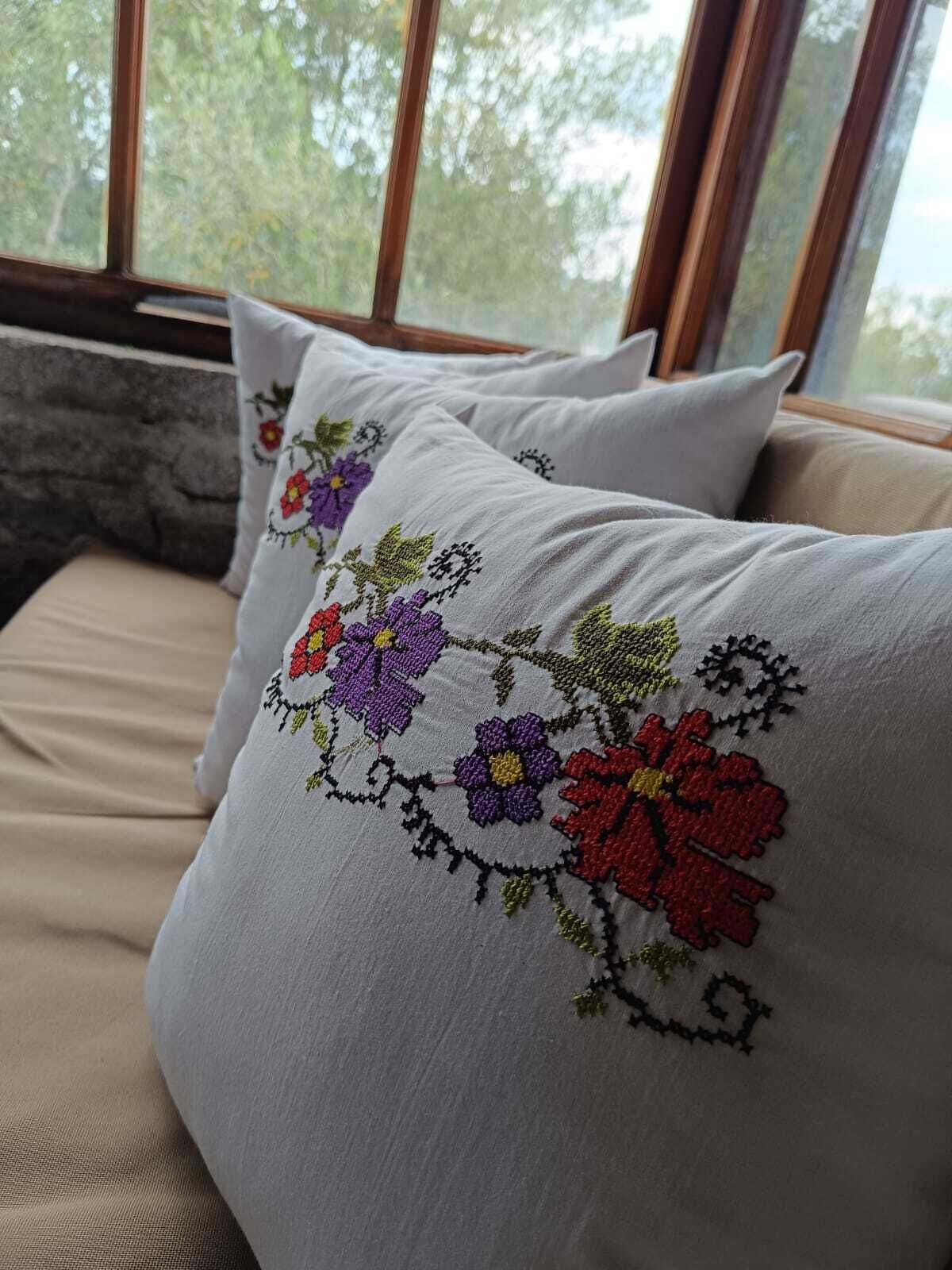 Ett fönster med utsikt över träd, en stenmur och två kuddar med broderade blommönster.