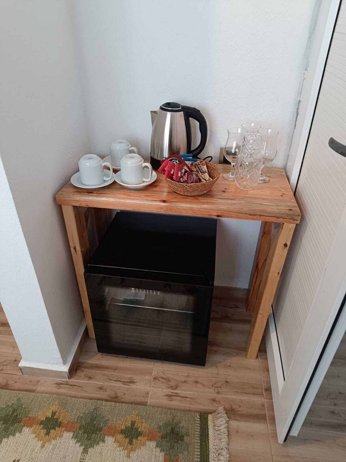A small wooden table with a coffee maker, cups, and a basket of snacks.