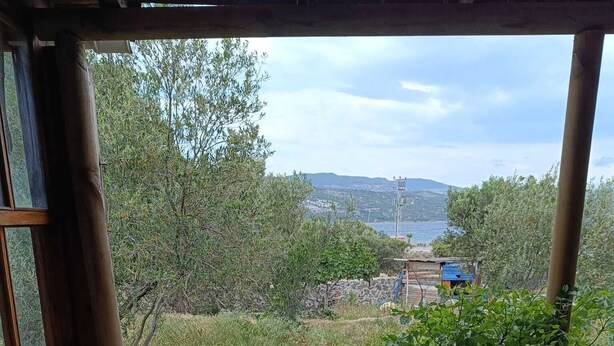 A wooden bench and a sofa with patterned cushions, overlooking a grassy area with trees and a distant view of a town. - Dilara Huzur Motel (Ayvacik)