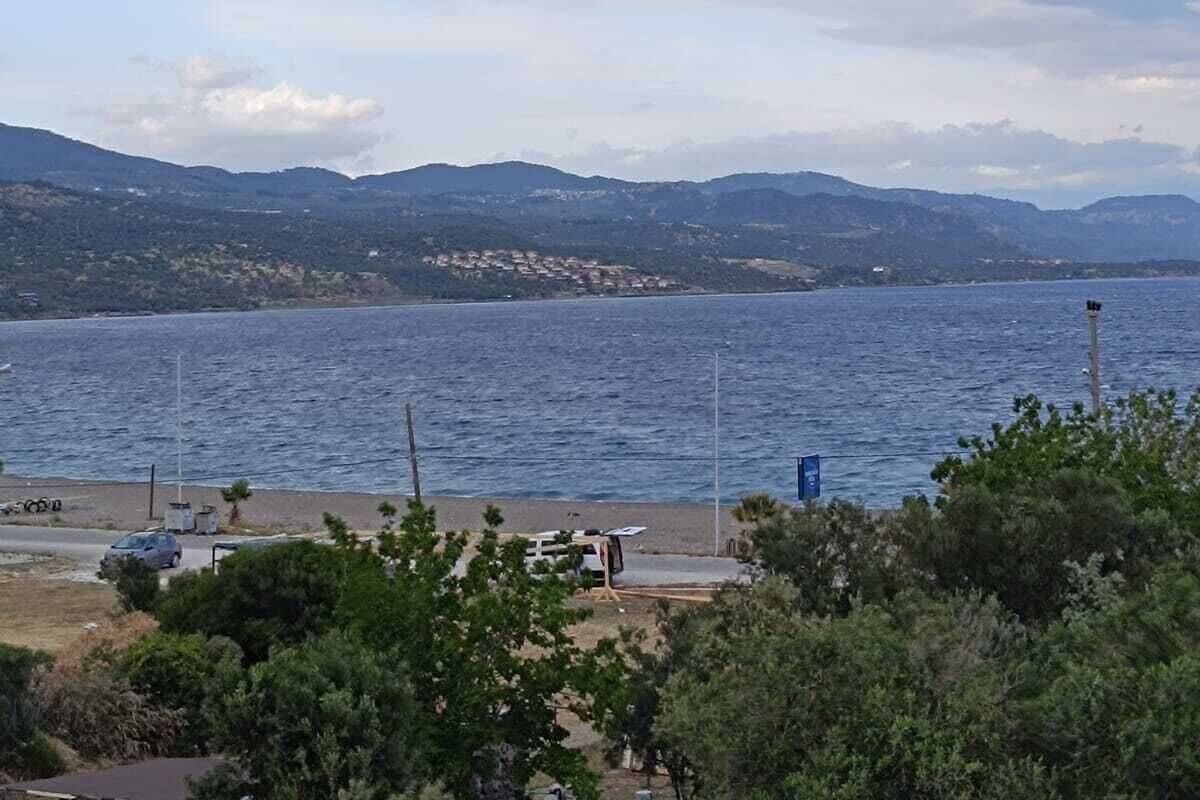 Vista costera con una masa de agua, montañas distantes y cielo despejado.