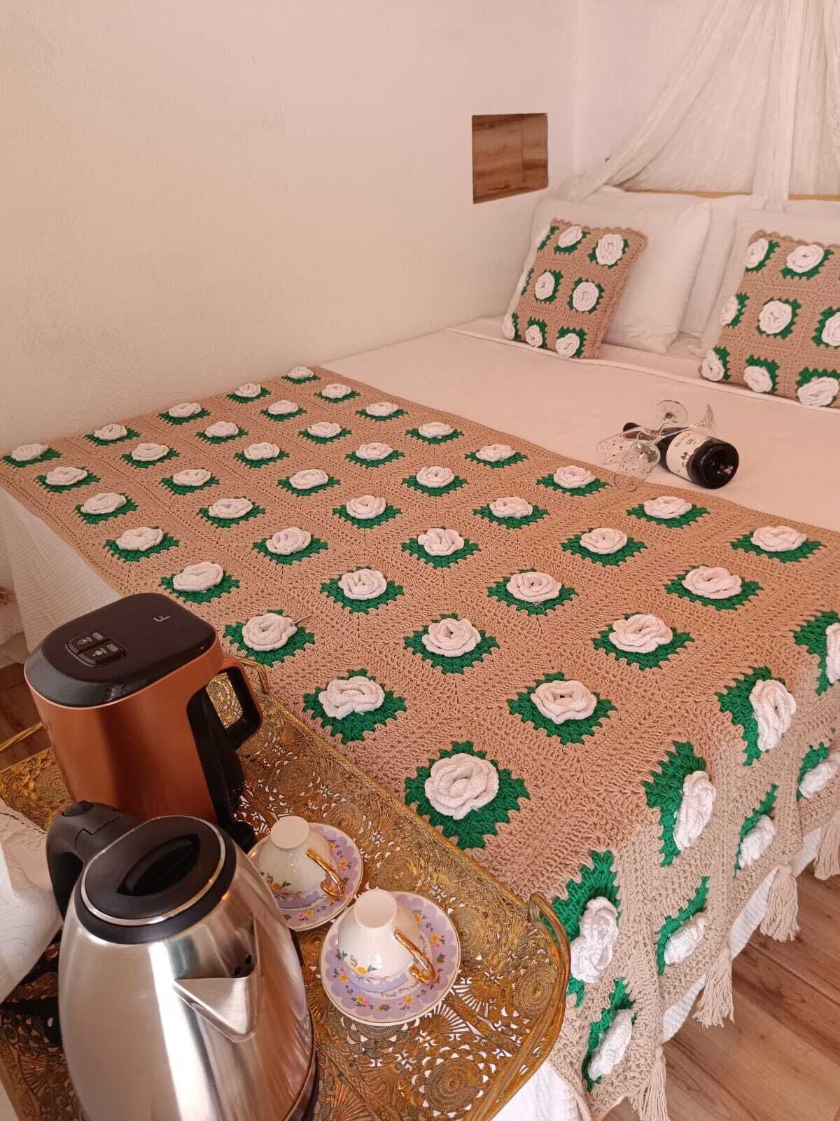 A neatly made bed with a patterned blanket, a coffee maker, a kettle, and a tray with teacups and saucers.