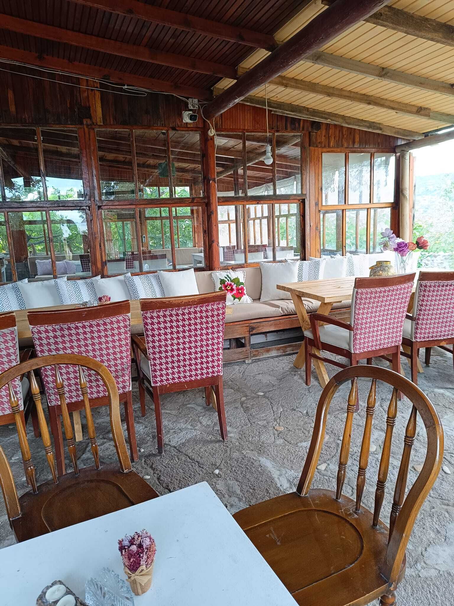 A rustic wooden interior with a high ceiling, large windows, and a mix of wooden and upholstered furniture.