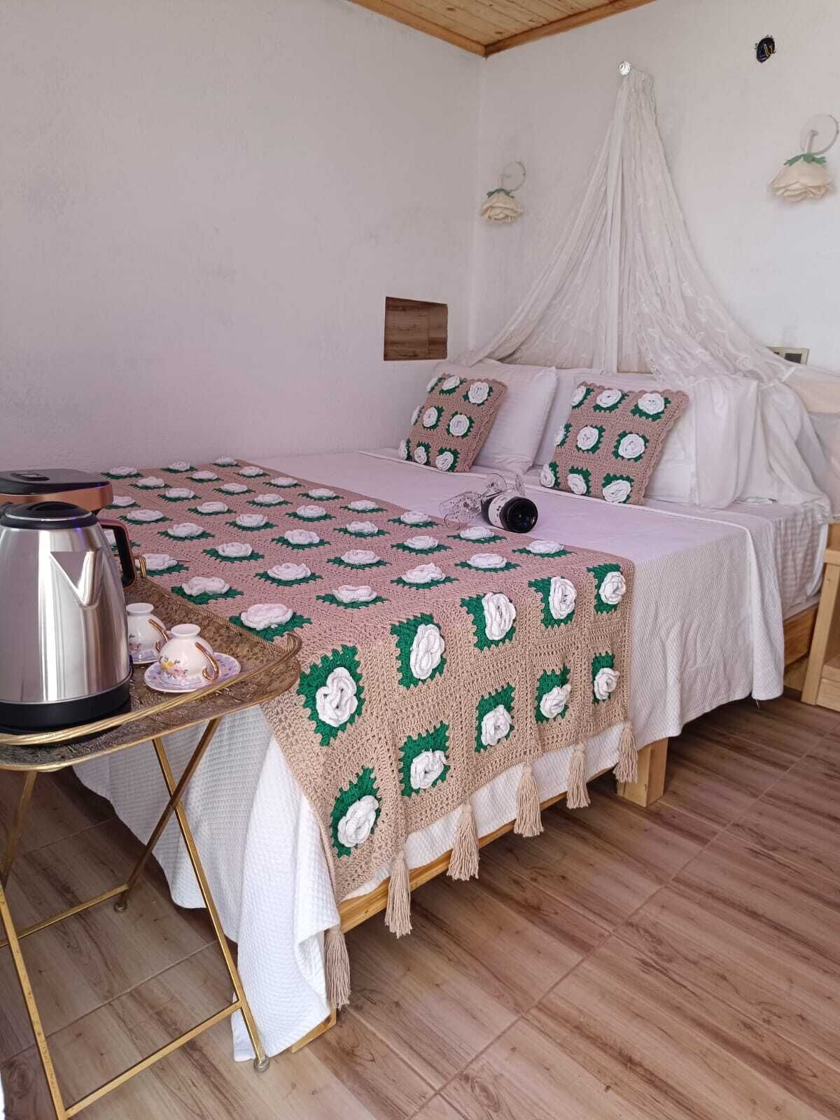 Une chambre confortable avec un lit à baldaquin, une table de chevet avec une bouilloire et des tasses, et une couverture à motifs.