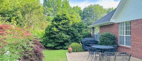A patio with a table and chairs, a barbecue grill, and a brick building.
