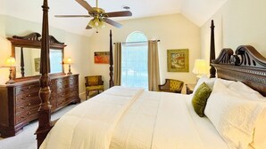 A bedroom with a large bed, a wooden dresser, a ceiling fan, and a window with curtains. - The Betty, 3BR Classic Home by Velvet Ditch Villas (Oxford)