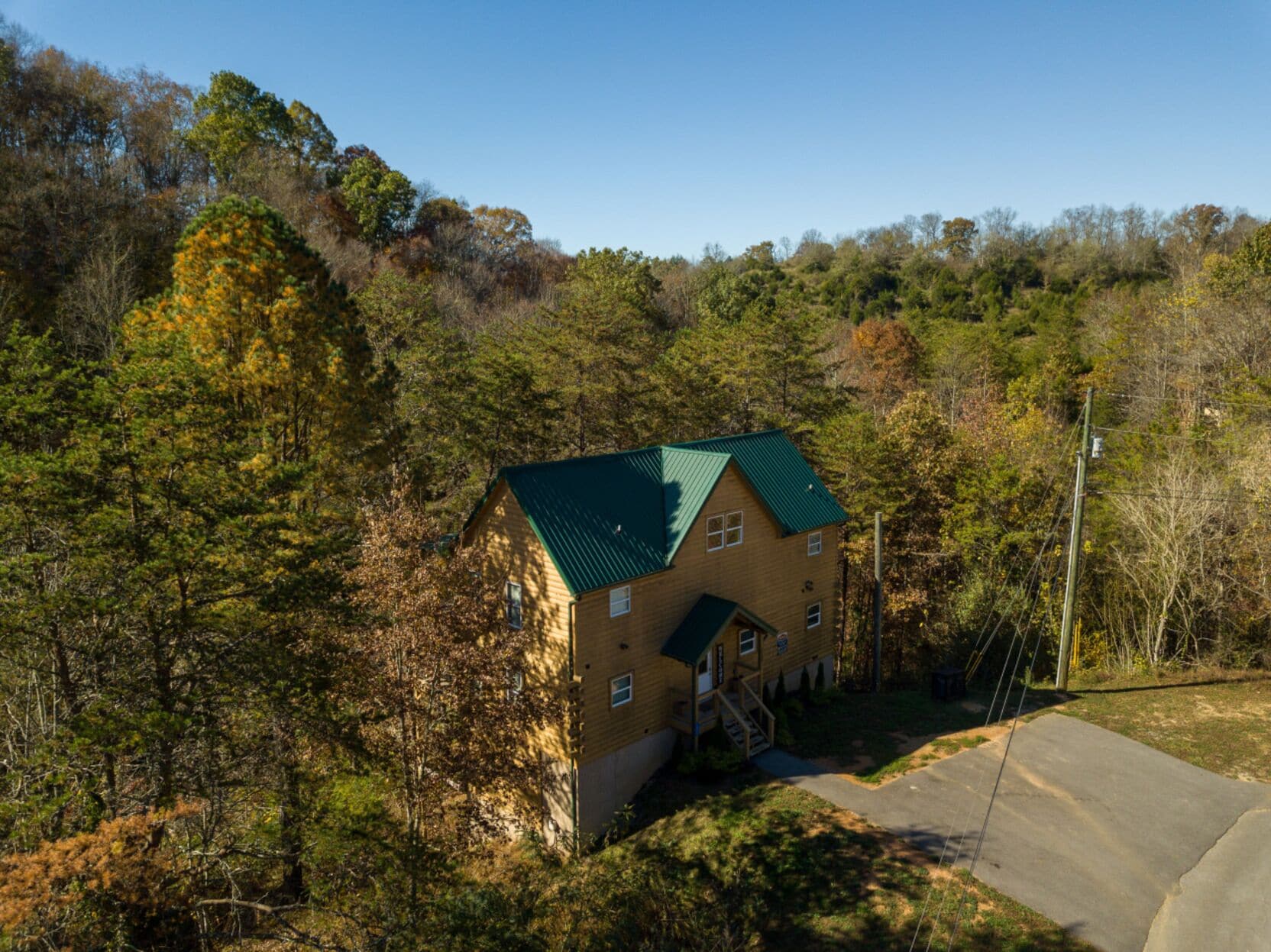 A two-story wooden cabin with a green roof, surrounded by dense forest.