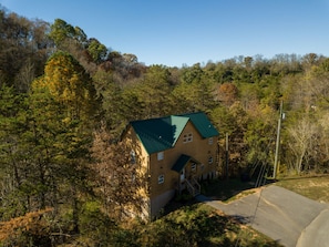 A two-story wooden cabin with a green roof, surrounded by dense forest.