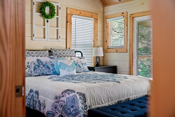 A bedroom with a bed, a nightstand, a lamp, a window with blinds, and a wooden wall. - Countryside Comfort By Ghosal Luxury Lodging (Sevierville)