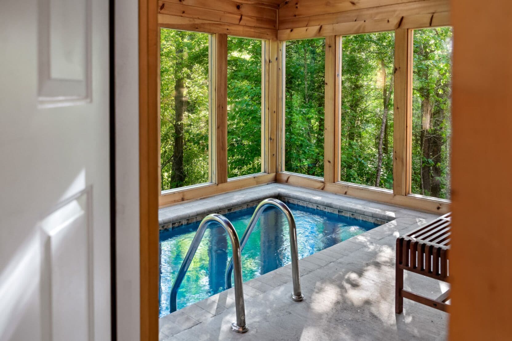 Eine Holzterrasse mit Pool und Sitzbank, umgeben von großen Fenstern mit Blick auf einen Wald.