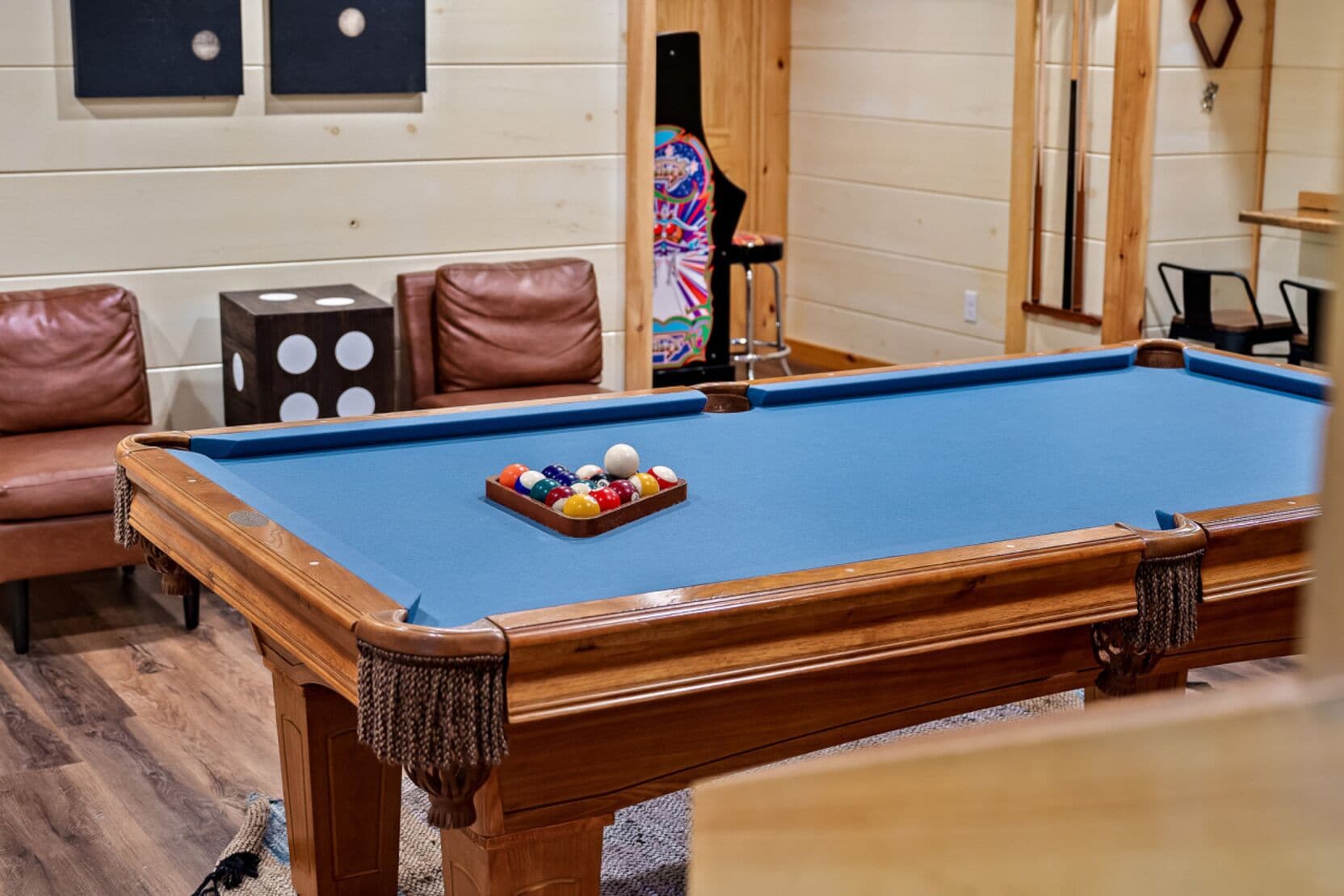 Une table de billard avec un jeu de billes, un fauteuil en cuir marron et un meuble en bois orné de motifs circulaires.