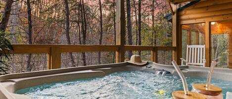 A hot tub with a wooden deck and a view of trees.