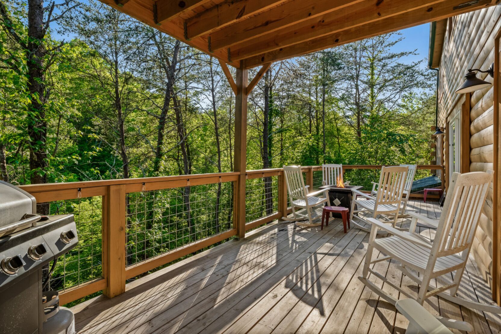 A wooden deck with a grill, chairs, and a fire pit.