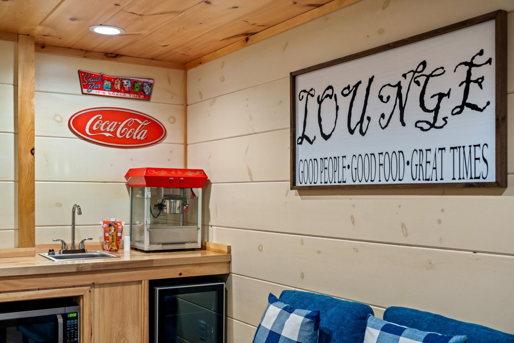 A cozy lounge area with a Coca-Cola sign, a snack bar sign, and a sign that reads "LOUNGE GOOD PEOPLE GOOD FOOD GREAT TIMES."