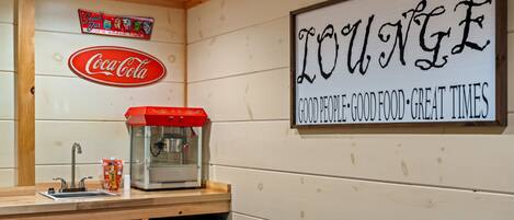 A cozy lounge area with a Coca-Cola sign, a snack bar sign, and a sign that reads "LOUNGE GOOD PEOPLE GOOD FOOD GREAT TIMES."