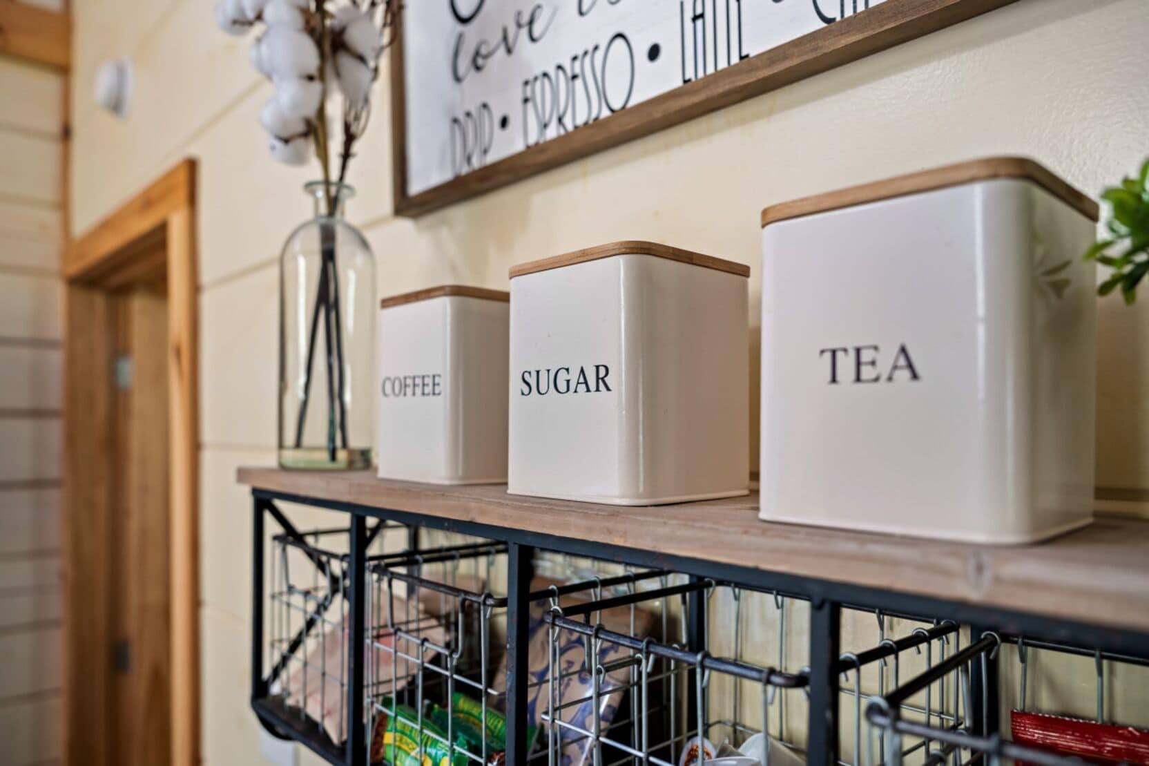 A shelf with labeled containers for coffee, sugar, and tea, and a sign above them.