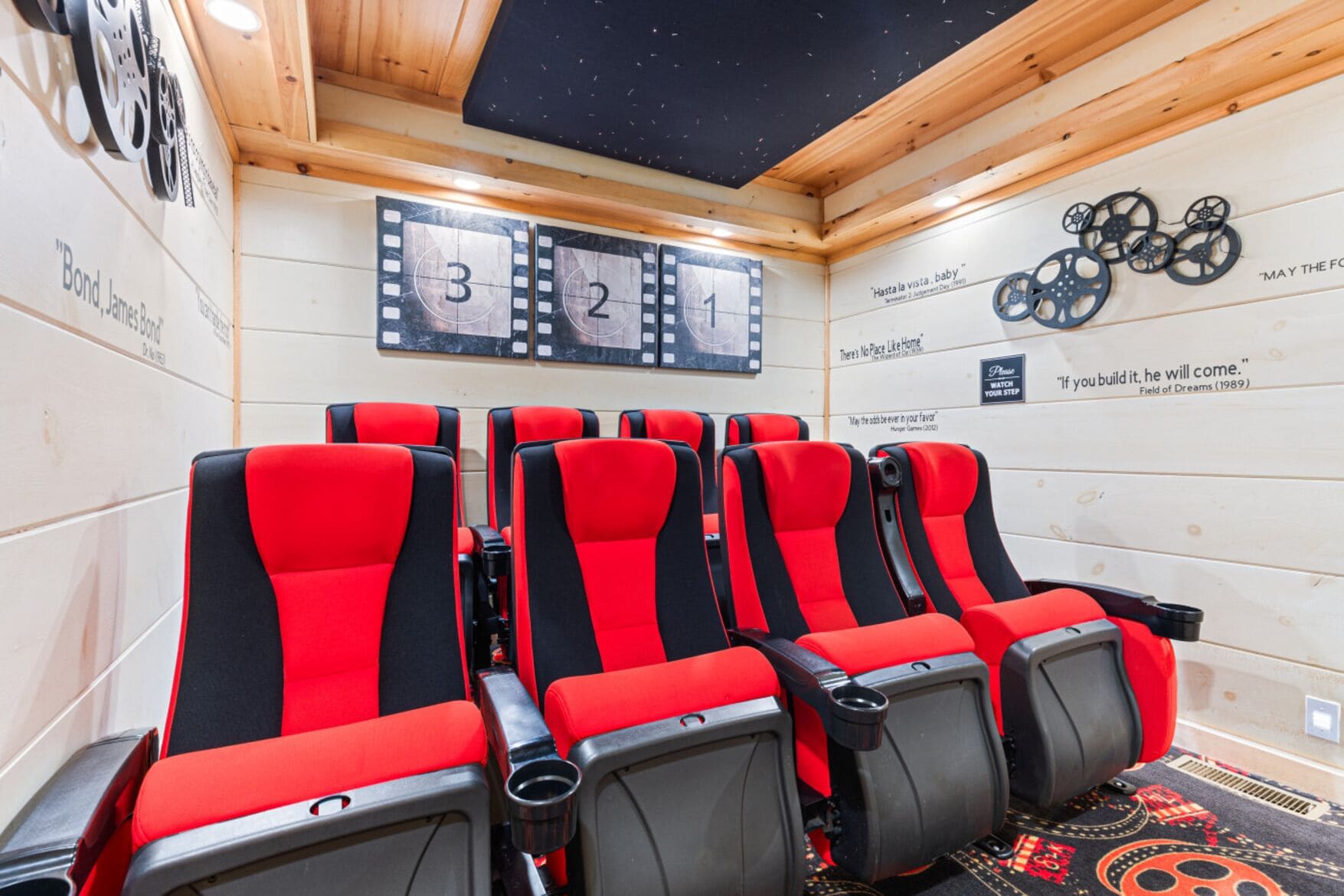 A room with four red and black cinema-style seats, a wooden ceiling, and a wall with filmstrip decorations and motivational quotes.