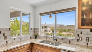 A kitchen with a large window, a sink, and wooden cabinets. - Modern Resort Condo - Pools, Courts & Scenic Views (St. George)