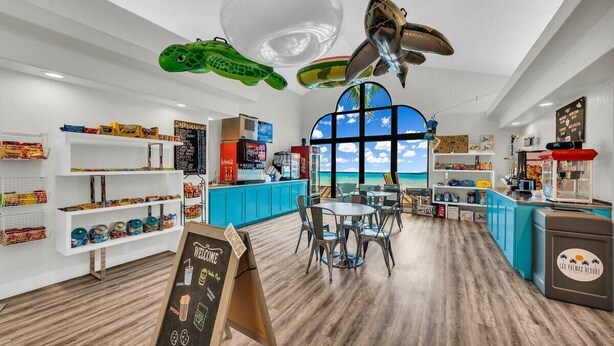 A restaurant with a view of the ocean, featuring a wooden floor, blue counter, and various food items on display. - Modern Resort Condo - Pools, Courts & Scenic Views (St. George)