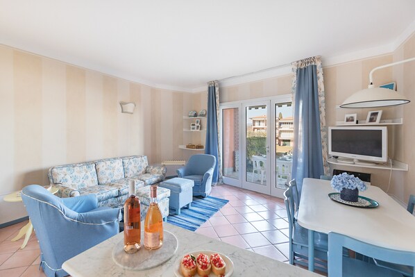 Un salon comprenant un canapé, des fauteuils, une table à manger avec un téléviseur, et un balcon avec vue.