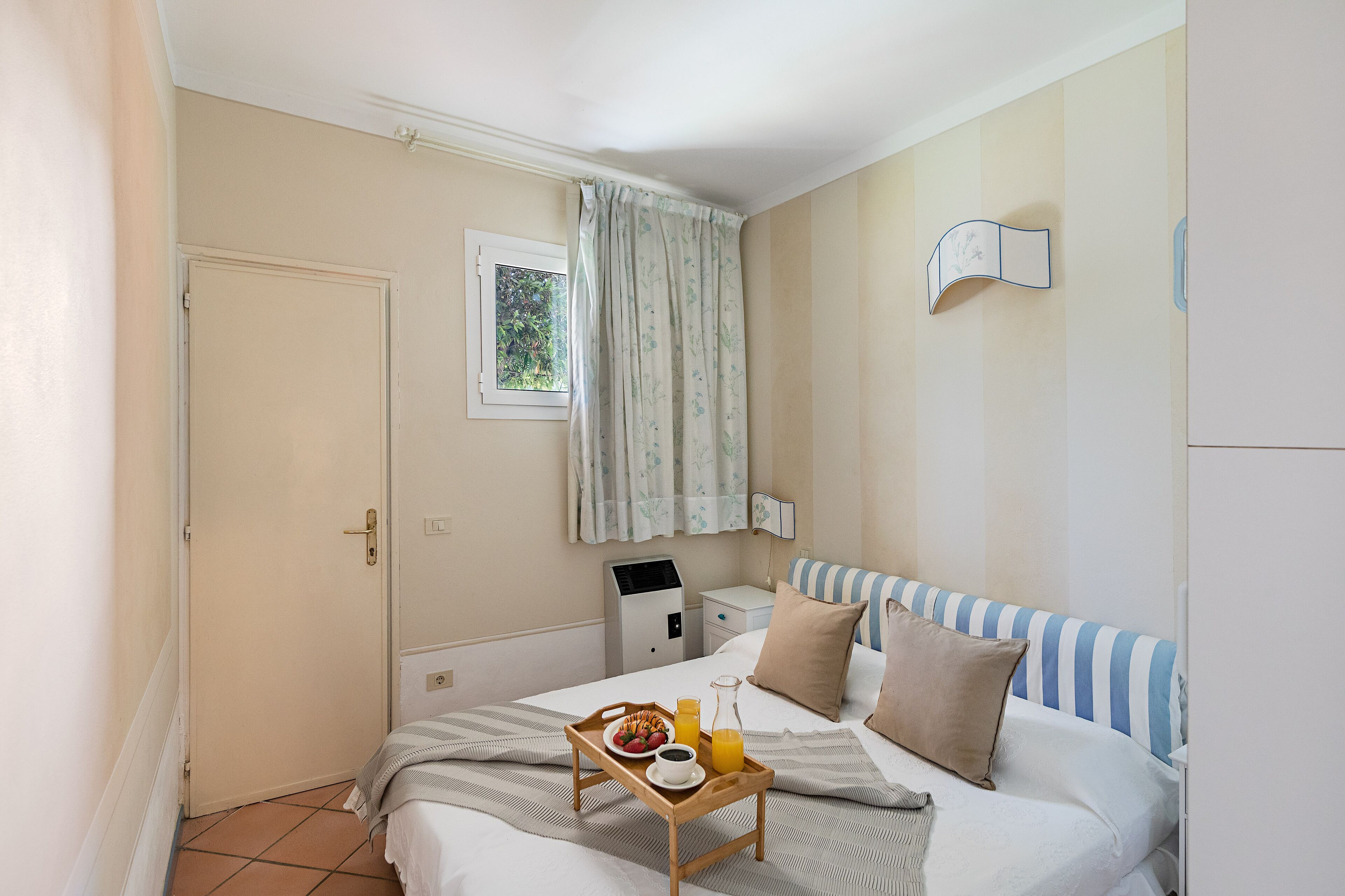A hotel room with a bed, a bedside table, a desk, and a window with curtains.