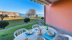 A terrace with a table set for dining, overlooking a body of water and a distant mountain range. - San Sivino 142 Apartment by Wonderful Italy (Manerba del Garda)