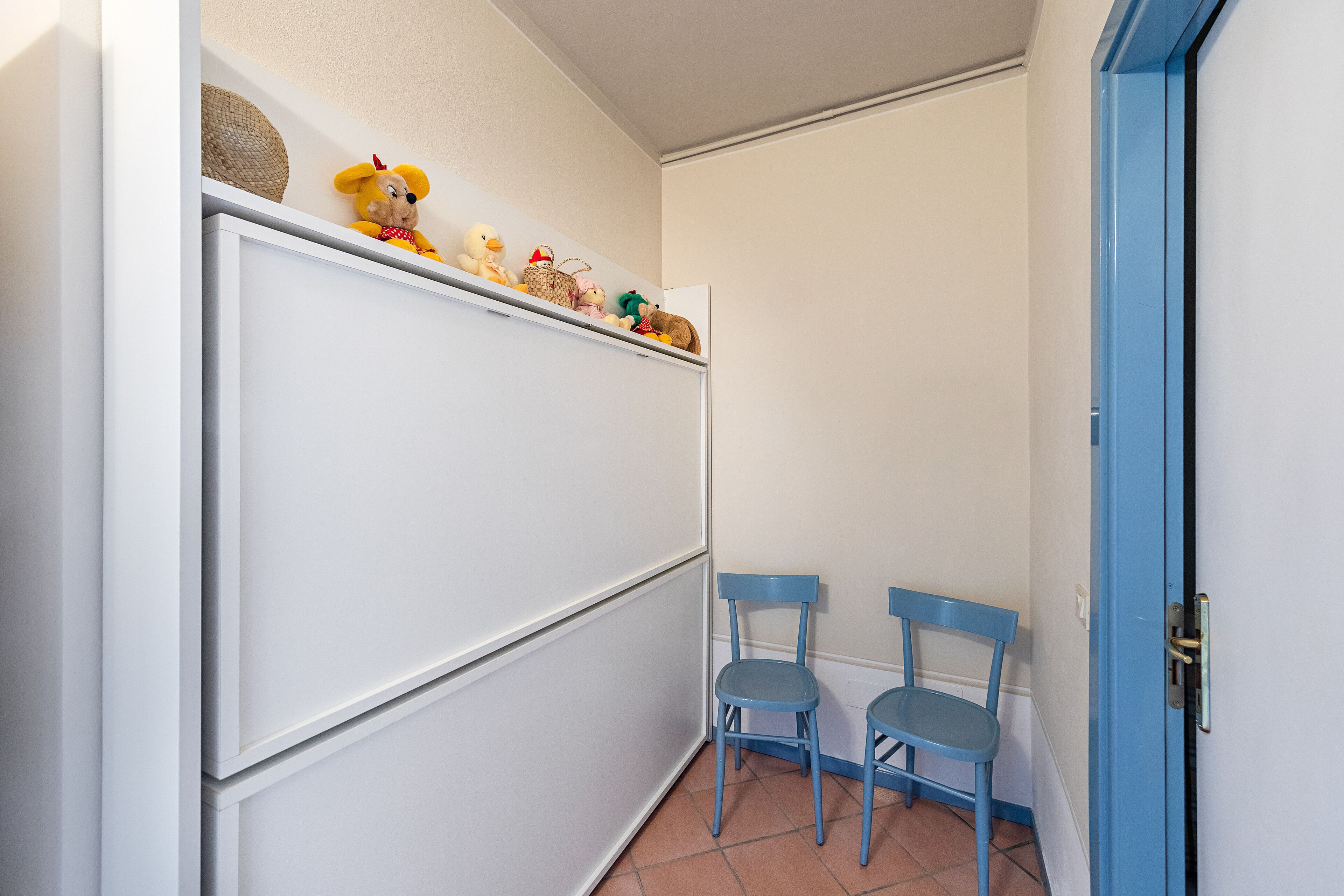 A room with a white cabinet, two blue chairs, and a blue door.