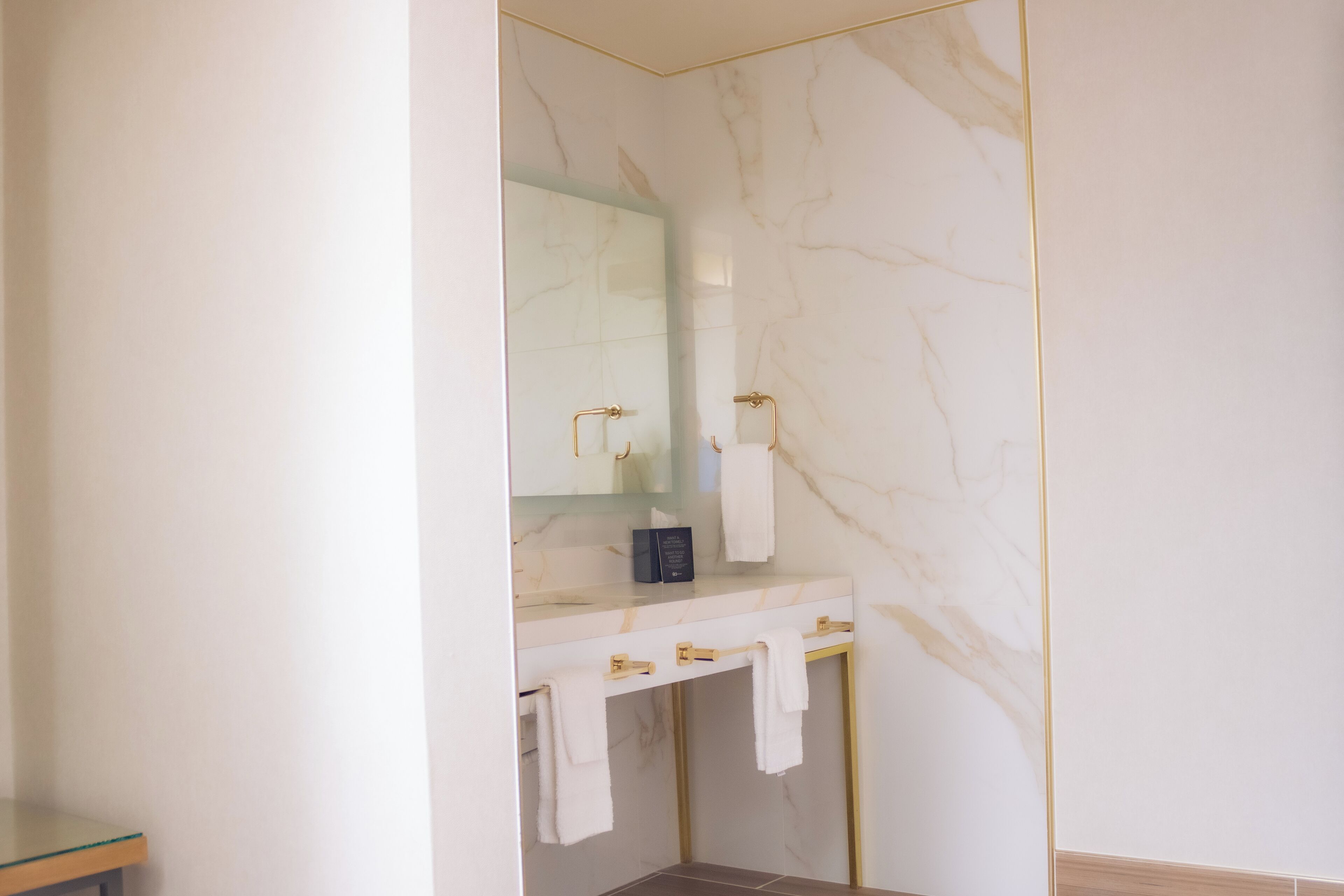 Un baño moderno con tocador de mármol, accesorios dorados y cabina de ducha de vidrio.