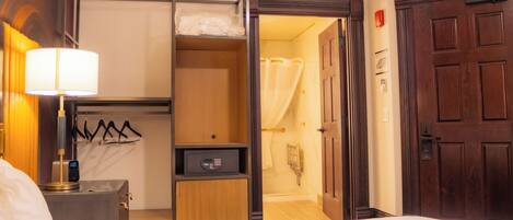 A hotel room with a bed, a bedside table with a lamp, a wardrobe, and a bathroom visible through an open door.