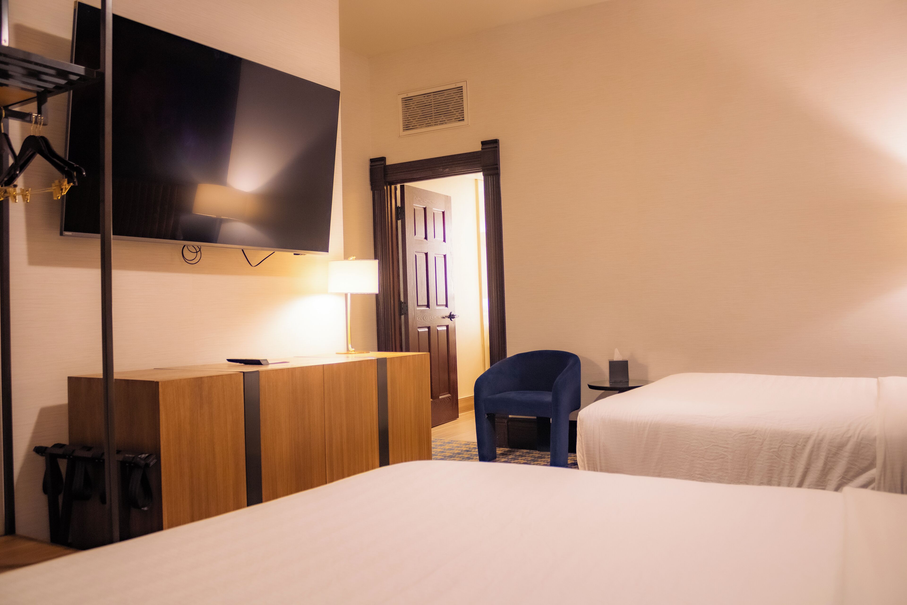 A hotel room with two beds, a desk with a flat-screen TV, a chair, and a lamp.