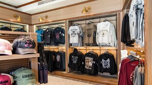 En tøjbutik med træhylder og stativer, der viser forskellige T-shirts og hættetrøjer.