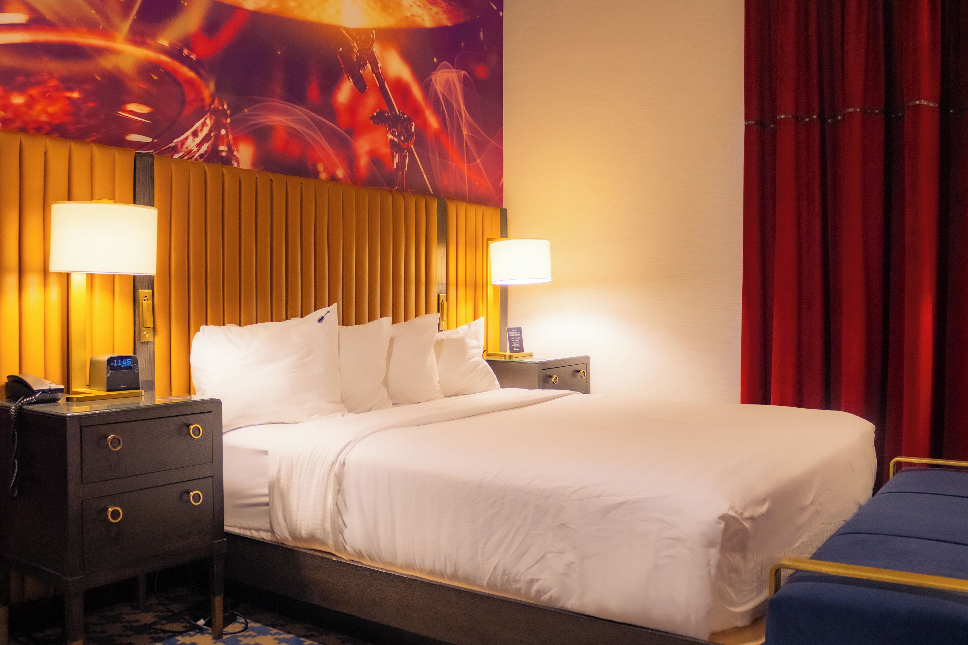 A hotel room with a large bed, two bedside tables, a nightstand, and a wall mural.