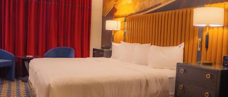 A hotel room with a large bed, two bedside tables with lamps, a desk with a chair, and a red curtain.