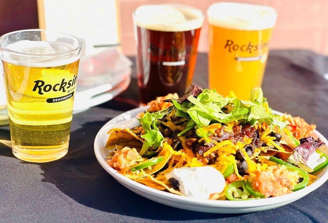 A plate of nachos with various toppings and three glasses of beer.