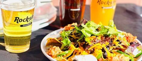 Un plato de nachos con diferentes ingredientes y tres vasos de cerveza.