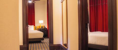 A hotel room with a checkered floor, a bed, a nightstand, a mirror, and red curtains.