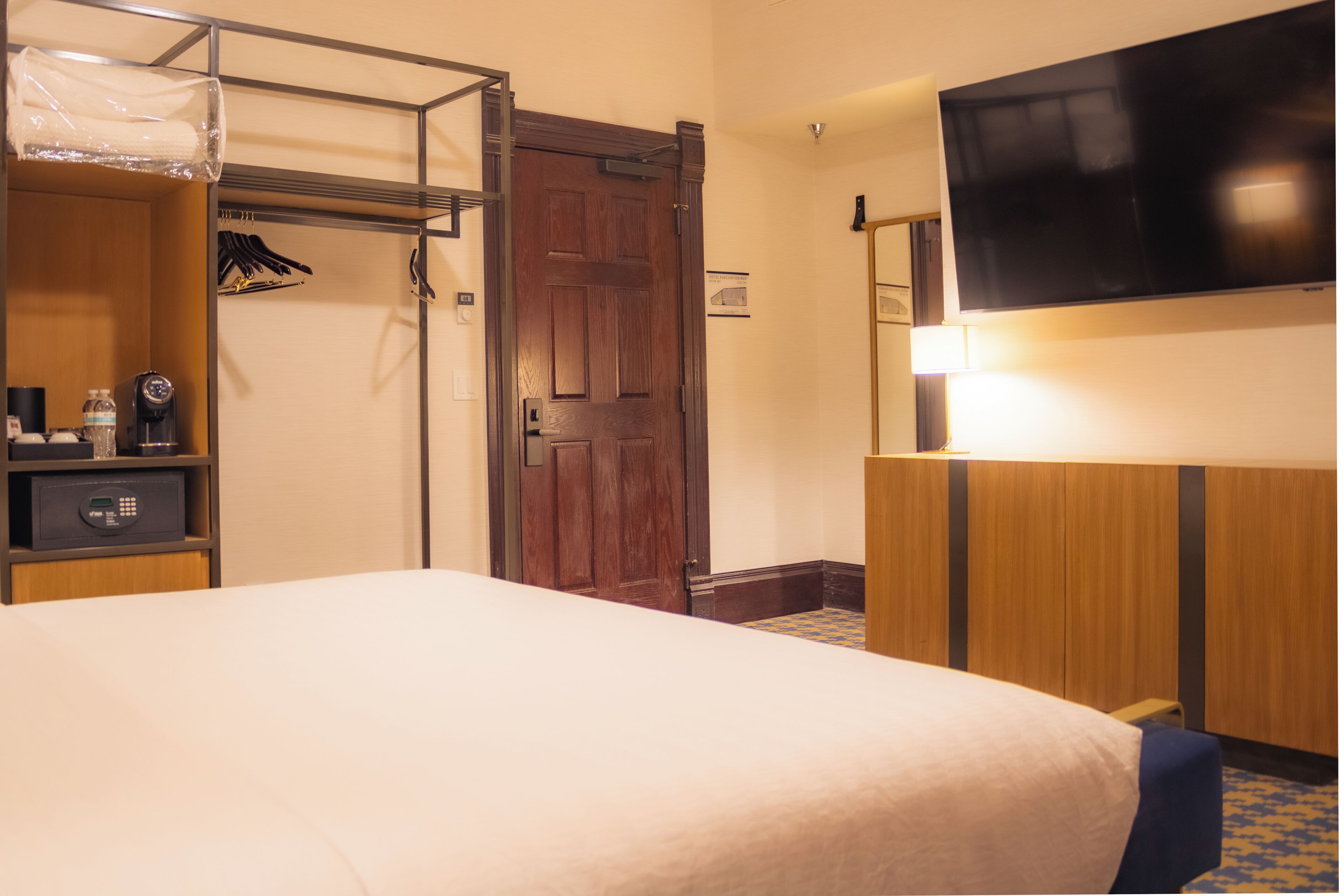 A hotel room with a bed, a wardrobe, a desk with a chair, a television, and a door.