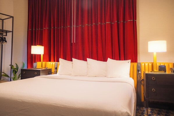 Een hotelkamer met een groot bed, rode gordijnen, twee bedlampen en een nachtkastje met een klok.