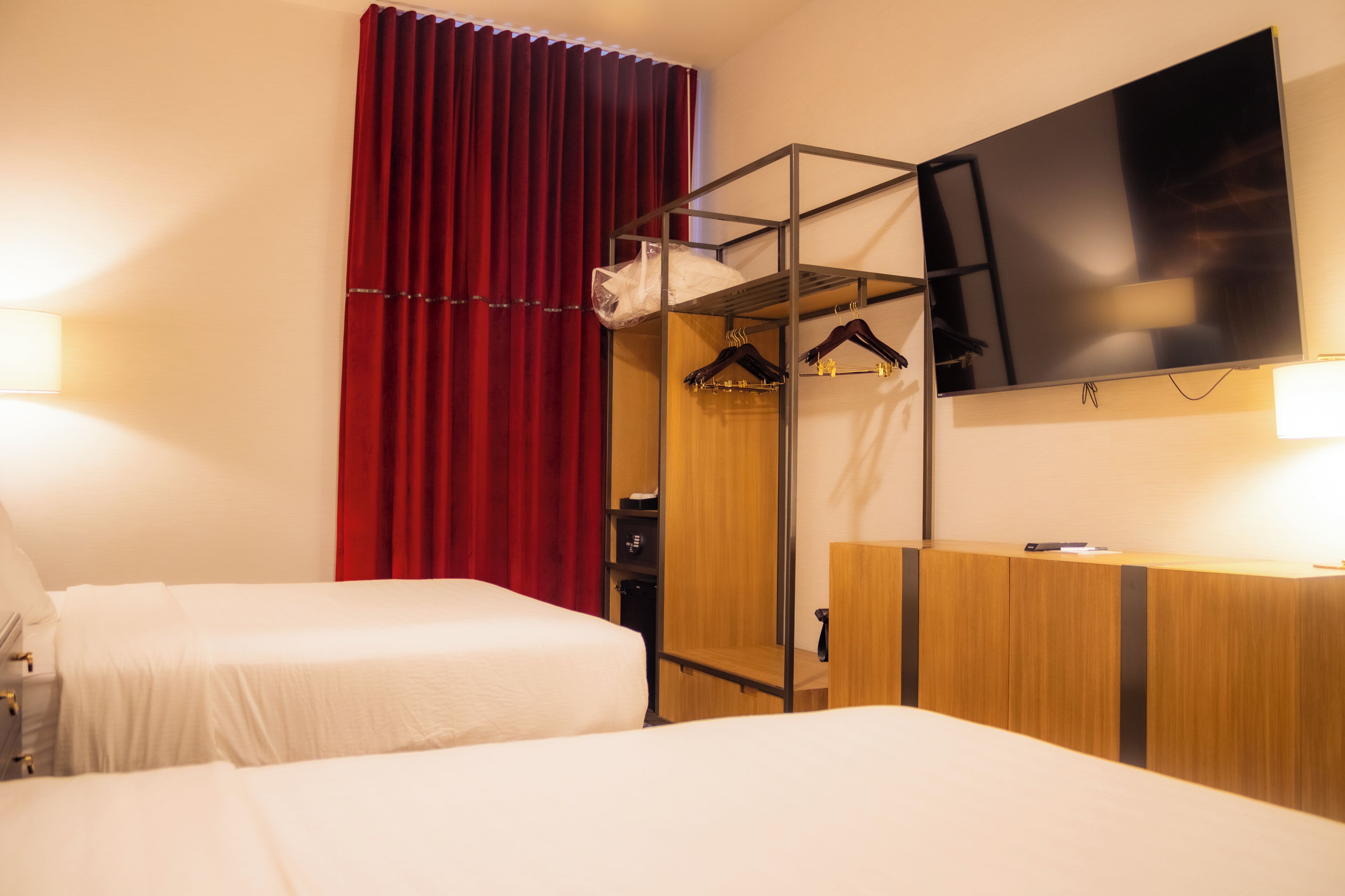 Camera d'albergo con due letti, una TV a parete, un armadio e una tenda rossa.