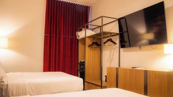 A hotel room with two beds, a TV mounted on the wall, a wardrobe, and a red curtain.