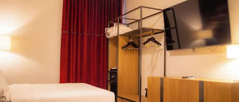 Camera d'albergo con due letti, una TV a parete, un armadio e una tenda rossa.