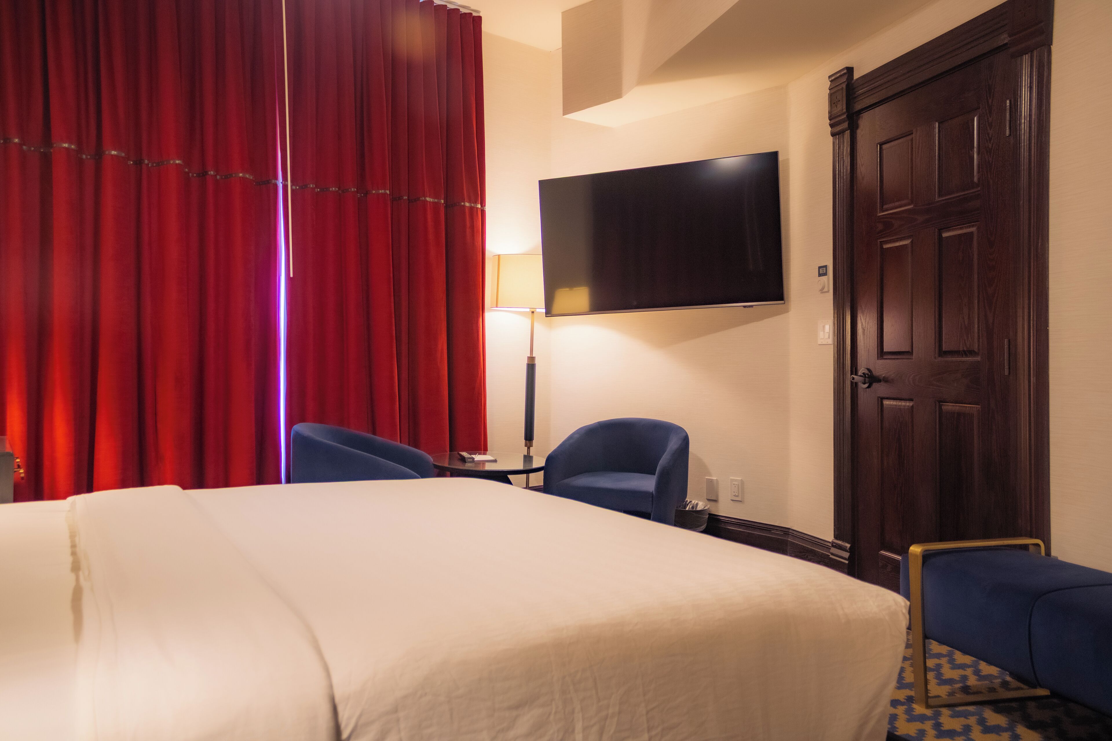 A hotel room with a bed, two chairs, a TV, and a door.