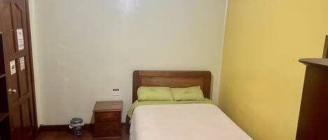 A bedroom with a wooden bed, a nightstand, a dresser, and a door with a sign.