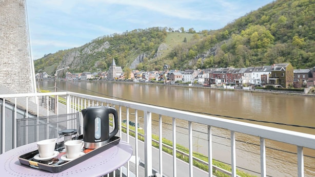Uma varanda com uma bandeja de chá, chaleira e vista para um rio, edifícios e uma colina ao fundo.