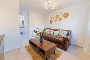 A modern living room with a brown leather sofa, a wooden coffee table, and a vase with plants.