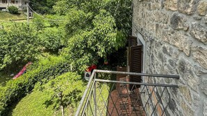 Un bâtiment en pierre doté d’un balcon donnant sur un jardin luxuriant et une colline.