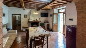 Un intérieur rustique avec des poutres apparentes, une cheminée, une table à manger avec des chaises et un coin cuisine.