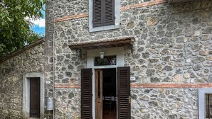 Un bâtiment en pierre avec une porte et des volets en bois, une petite fenêtre au-dessus de la porte et le numéro « 251 » inscrit sur le mur.