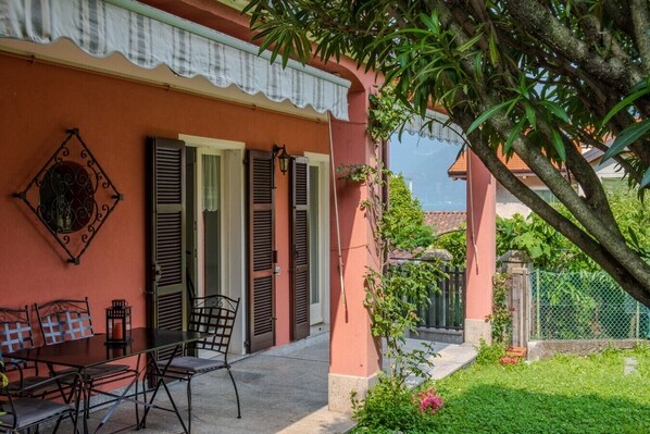 A building with a red exterior, a covered patio with chairs, and a small garden area.