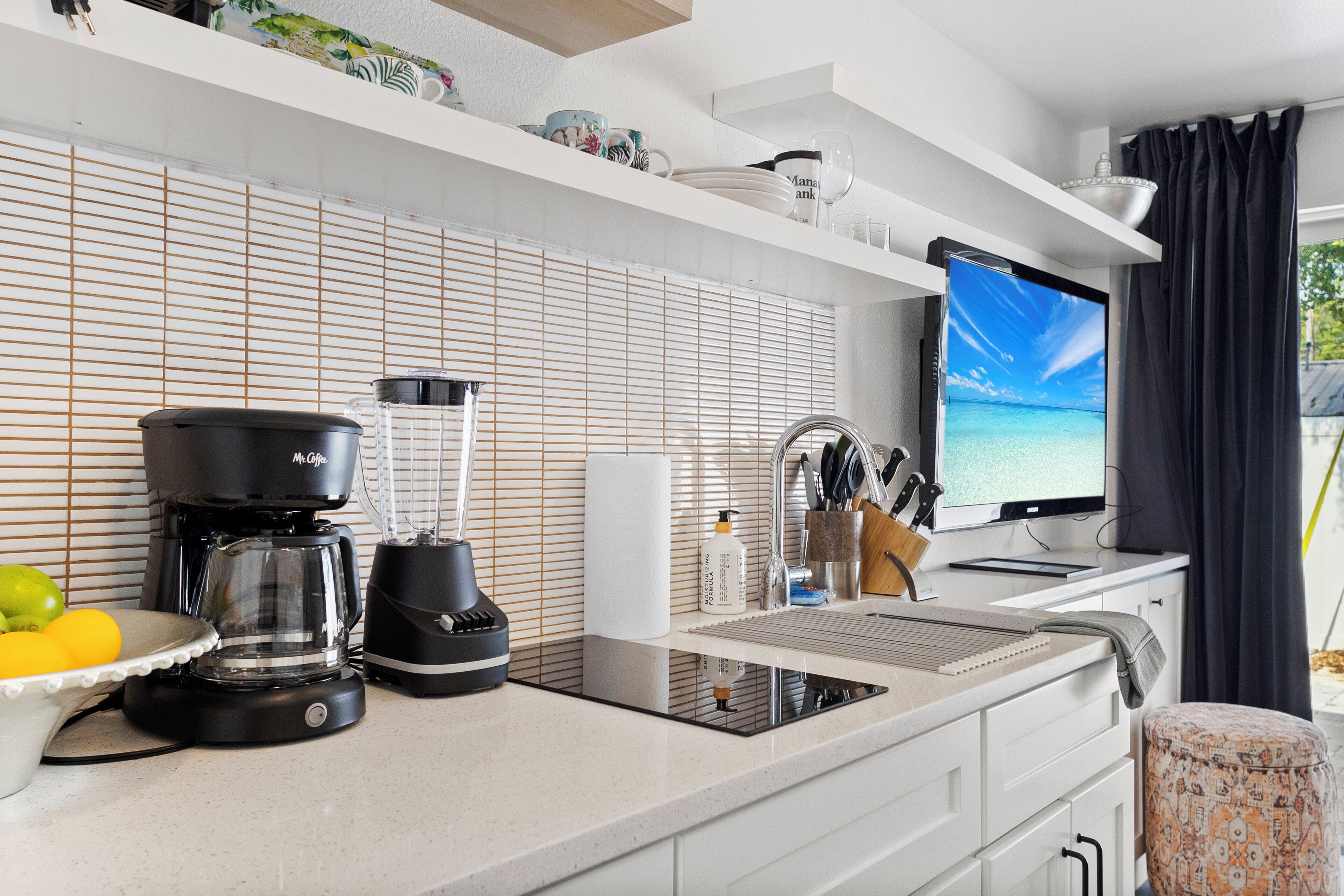 Une cuisine moderne équipée d’une cuisinière intégrée, d’une machine à café, d’un mixeur et d’un téléviseur à grand écran.
