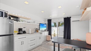 A modern kitchen with white cabinetry, a built-in microwave, and a large TV.